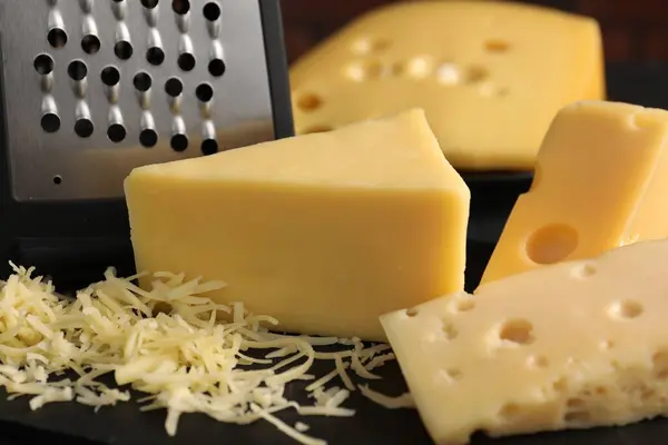 Grated, cut cheese and grater on black table, closeup