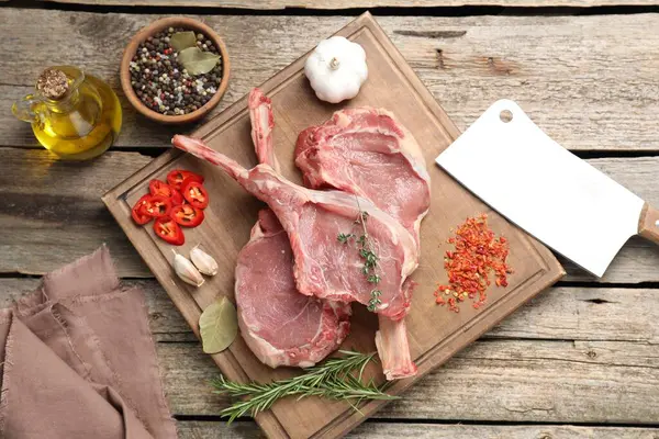 Fresh tomahawk beef cuts, butcher knife and spices on wooden table, top view