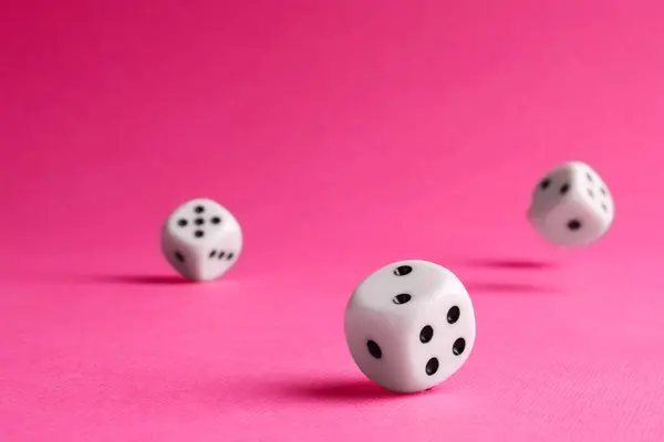 Many white game dices falling on pink background