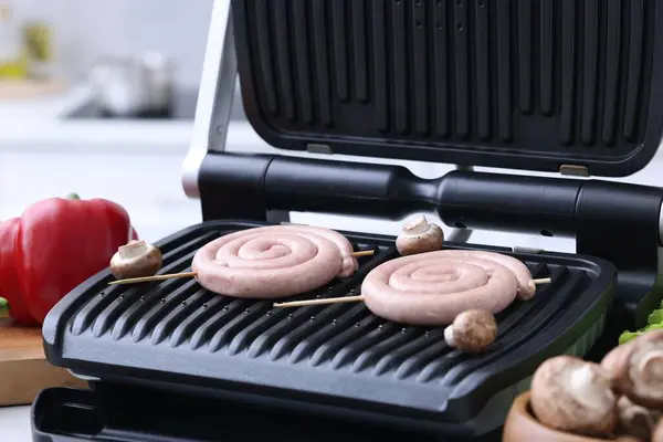 Electric grill with homemade sausages and mushrooms on table, closeup