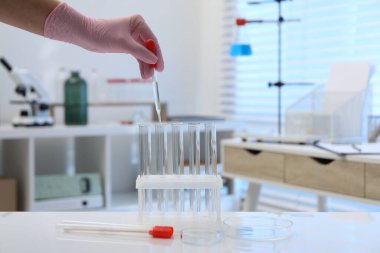 Laboratuvar analizi. Beyaz masada test tüplerine sıvı damlatan bir kadın, yakın plan.