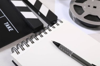 Film alkışı, film makarası, defter ve kalem ışık masasında.