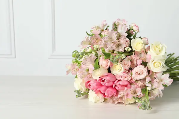Beautiful bouquet of fresh flowers on table near white wall. Space for text