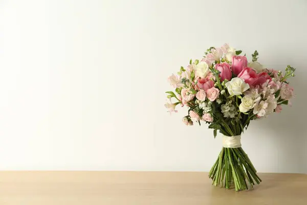 Beautiful bouquet of fresh flowers on wooden table near light wall. Space for text