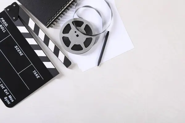 Movie clapper, film reel, notebook, sheet and pen on light textured table, flat lay. Space for text
