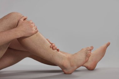 Gri arka planda bacak ağrısı çeken adam, yakın plan.