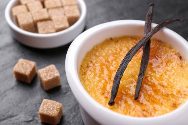 Lezzetli creme brulee kasede, vanilya kabukları ve şeker küpleri koyu gri masada, yakın plan.