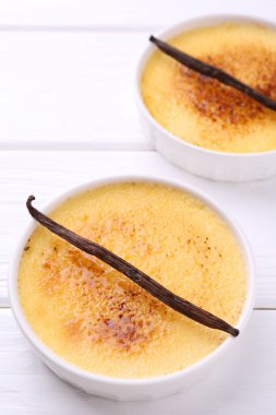 Lezzetli creme brulee kaseler ve beyaz ahşap masa üzerinde vanilya kabukları