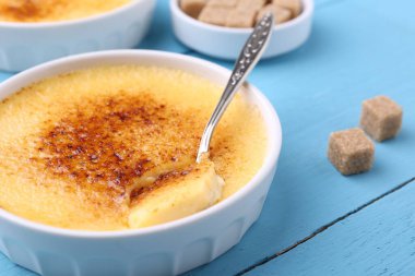 Lezzetli creme brulee kasede, şeker küpleri ve kaşık açık mavi ahşap masada, yakın plan