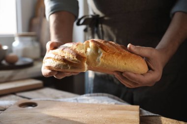 İçerideki ahşap masada ekmek kıran adam, yakın plan.