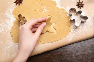 Ahşap masada kesicilerle Noel kurabiyesi yapan kadın.