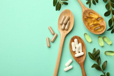 Farklı vitamin kapsülleri kaşık ve yapraklarda turkuaz arka planda, düz yerde. Metin için boşluk