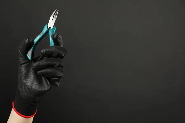 Woman with bent nose pliers on dark background, closeup. Space for text