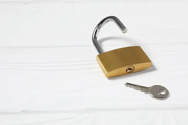 Steel padlock with key on white wooden table. Space for text