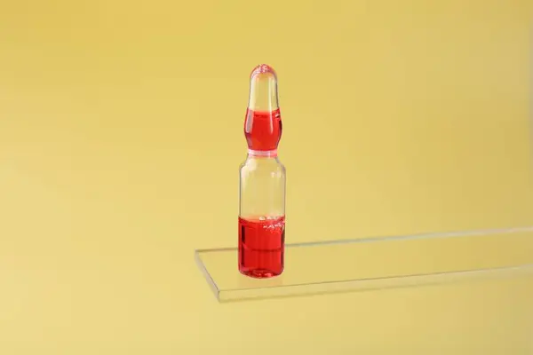 Glass ampoule with liquid on yellow background