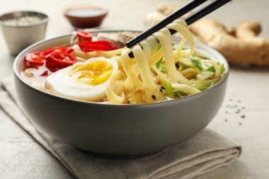 Loş masada çubuklarla lezzetli ramen yemek, yakın plan. Erişte çorbası.
