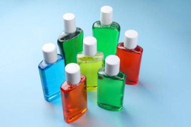 Fresh mouthwashes in bottles on light blue background clipart