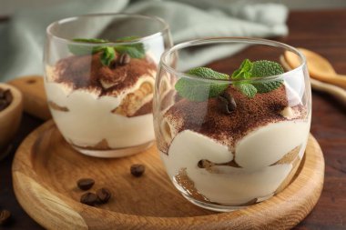 Bardakta nefis tiramisu, nane yaprakları ve ahşap masada kahve çekirdekleri, yakın plan.