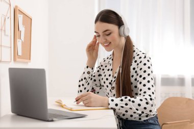 E-öğrenme. İçerideki masada online ders sırasında dizüstü bilgisayar kullanan genç bir kadın.