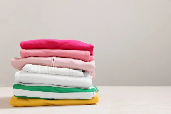 Stack of folded clothes on white table against grey background, space for text