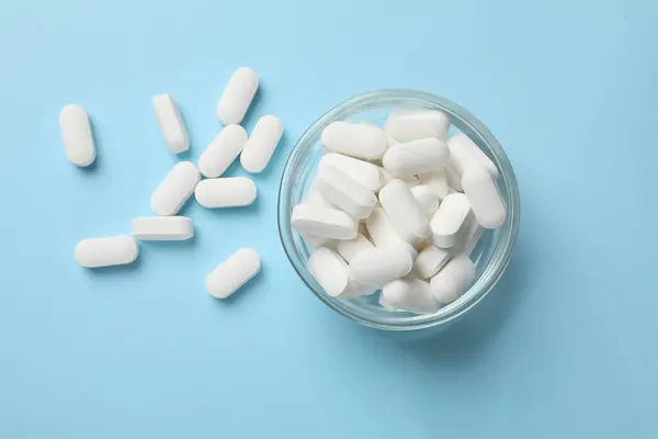 Vitamin capsules in bowl on light blue background, top view