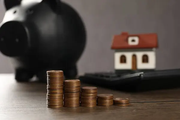 House model, piggy bank, calculator and stacked coins on wooden table, selective focus