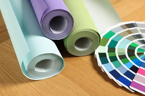Different wallpaper rolls and color palette samples on wooden table