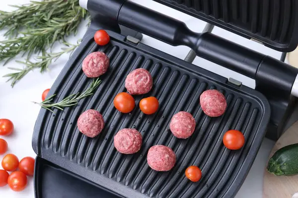 Electric grill with meatballs, tomatoes and rosemary on white table, above view