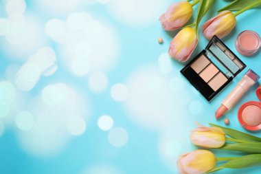 Farklı makyaj ürünleri ve açık mavi arkaplan üzerinde güzel lale çiçekleri. Metin için yer var, düz yatak. Bokeh etkisi