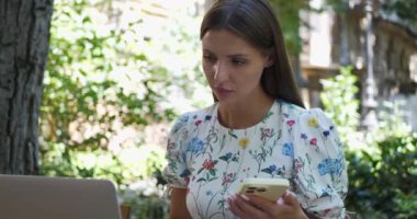 Dışarıda dizüstü bilgisayar ve akıllı telefon kullanan güzel bir kadın.