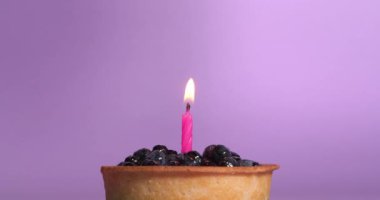 Mor arka planda yanan pembe mumlu yabanmersinli tart.