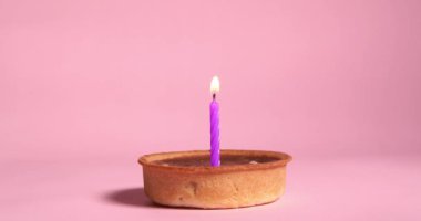 Pembe arka planda yanan menekşe şenlik mumlu karamel tartı.