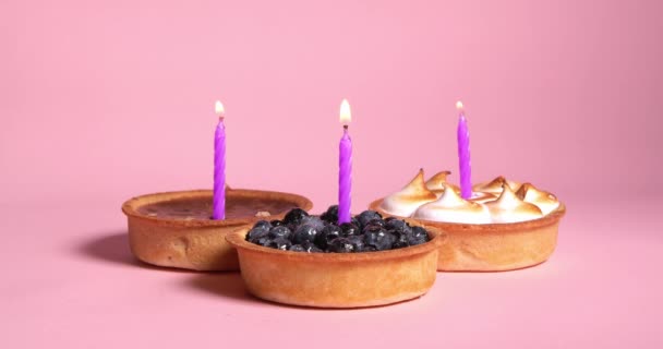 Diferentes Tartaletas Con Velas Festivas Violetas Ardientes Sobre Fondo Rosa — Vídeo de stock