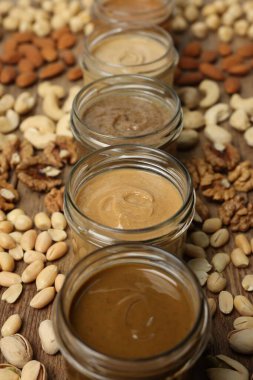 Nut butters in bowls and ingredients on wooden table, closeup clipart