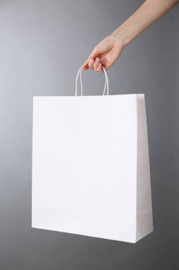 Gri arka planda beyaz kese kağıdı tutan kadın, yakın plan. Tasarım için model