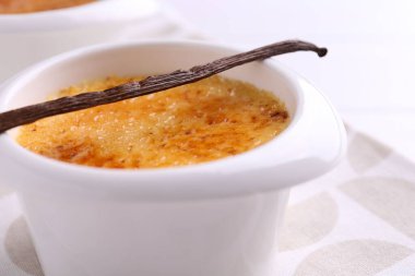 Lezzetli creme brulee kasede ve vanilya kapsülü masada, yakın plan
