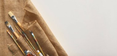 Doğal çuval bezi kumaşı ve beyaz arka planda farklı boya malzemeleri, üst manzara. Metin için boşluk