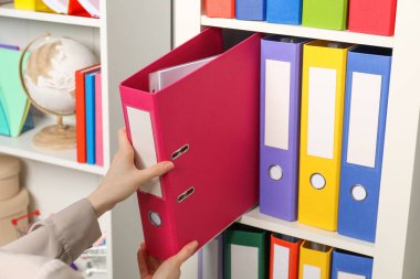 Kadın raflardan klasör ofis klasörünü alıyor, yakın plan.