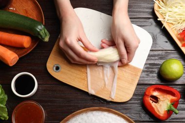 Lezzetli börek yapıyorum. Tahta masada taze sebzeleri pirinç kağıdına saran bir kadın.