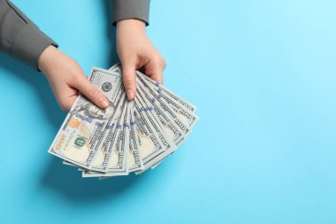 Para değişimi. Açık mavi arka planda bir kadının elinde dolar banknotları var. Metin için boşluk