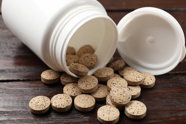 Bottle and vitamin pills on wooden table, closeup