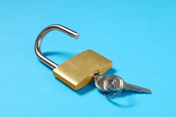 Steel padlock with keys on light blue background, closeup