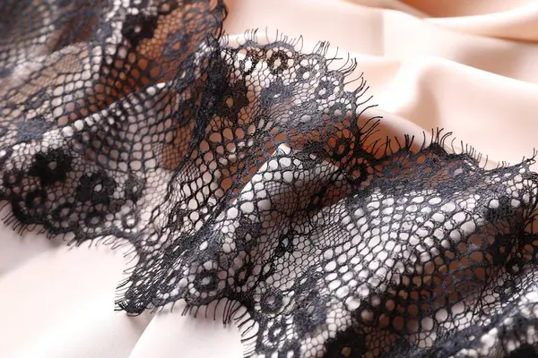 Beautiful black lace on beige fabric, closeup
