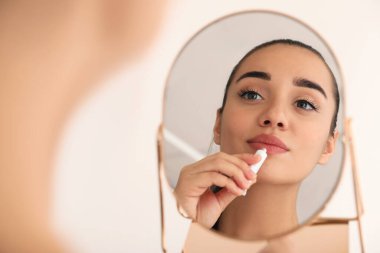 Genital uçuklu bir kadın, aynanın önünde, arka planda ışığa karşı krem sürüyor.