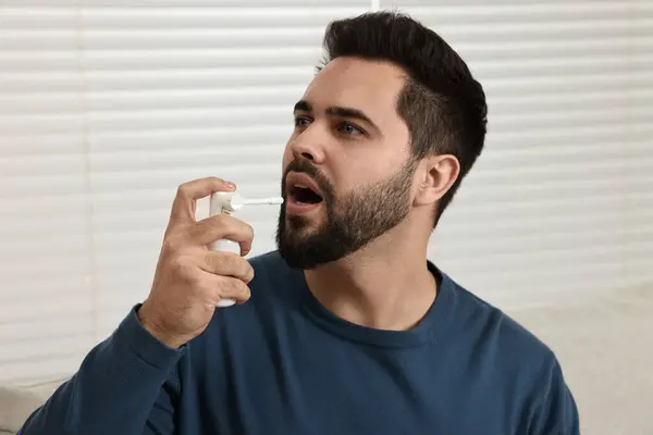 stock image Young man using throat spray at home