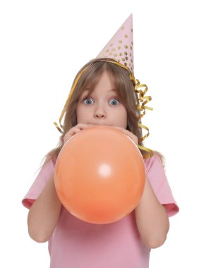 Beyaz arka planda balon şişiren parti şapkalı şirin küçük kız.