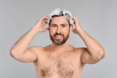 Saçını gri arka planda şampuanla yıkayan mutlu bir adam.
