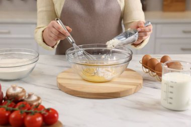 Kadın yumurtaları çırpıyor ve açık mermer masada una un ekliyor, yakın plan.