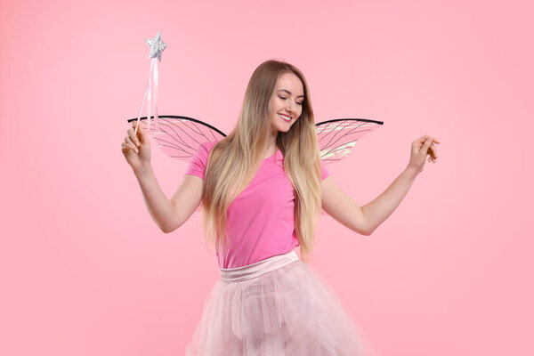 Beautiful girl in fairy costume with wings and magic wand on pink background