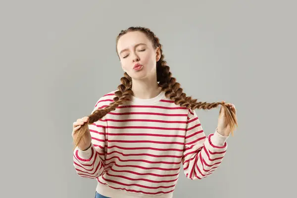 Woman with braided hair sending air kiss on grey background